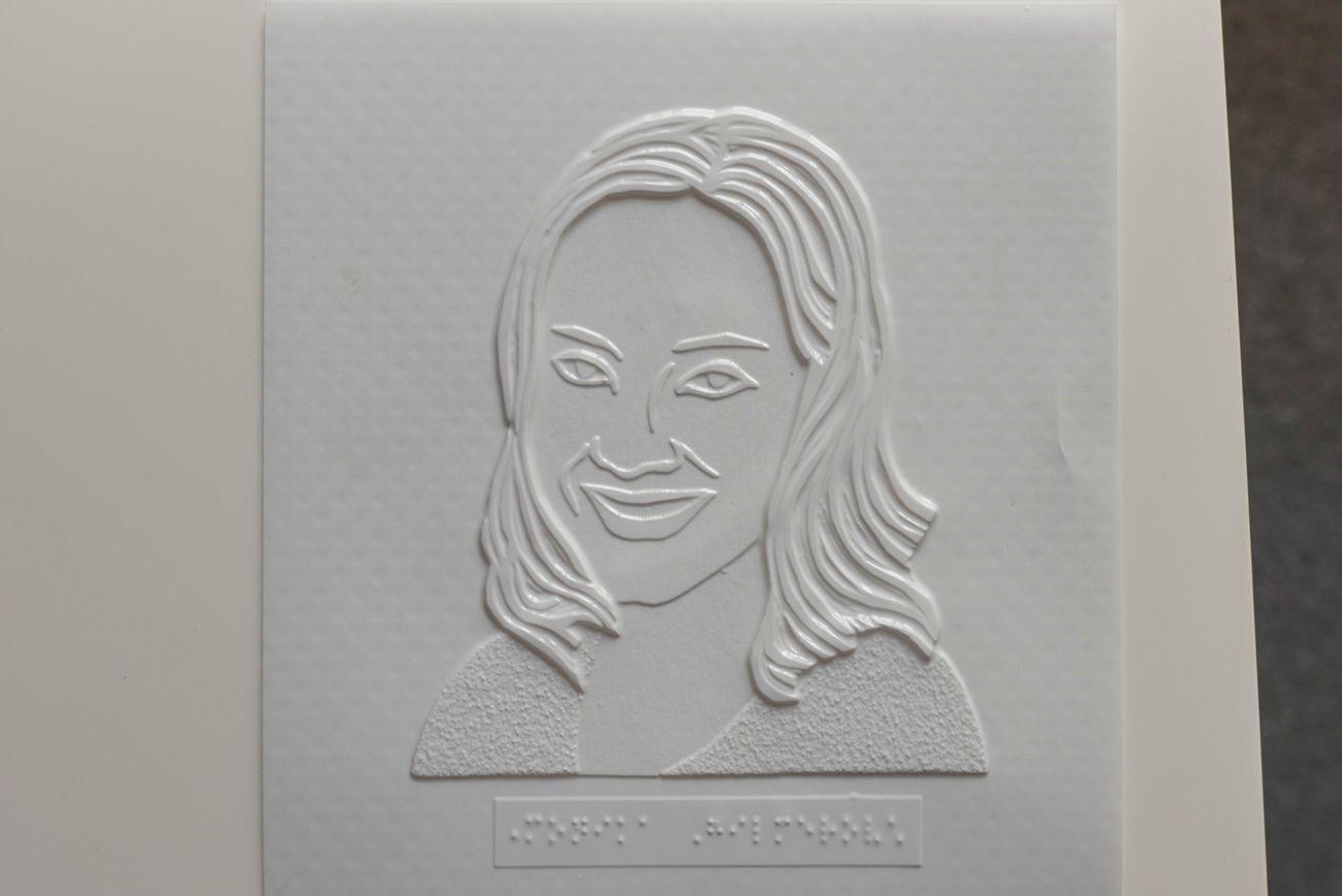 Popis fotgrafie: Na plastovej makete je pomocou 3D tlačiarne vytlačený obrys ženy, ktorý sa dá ohmatať. Pod obrázkom je popis v Braillovom písme.
